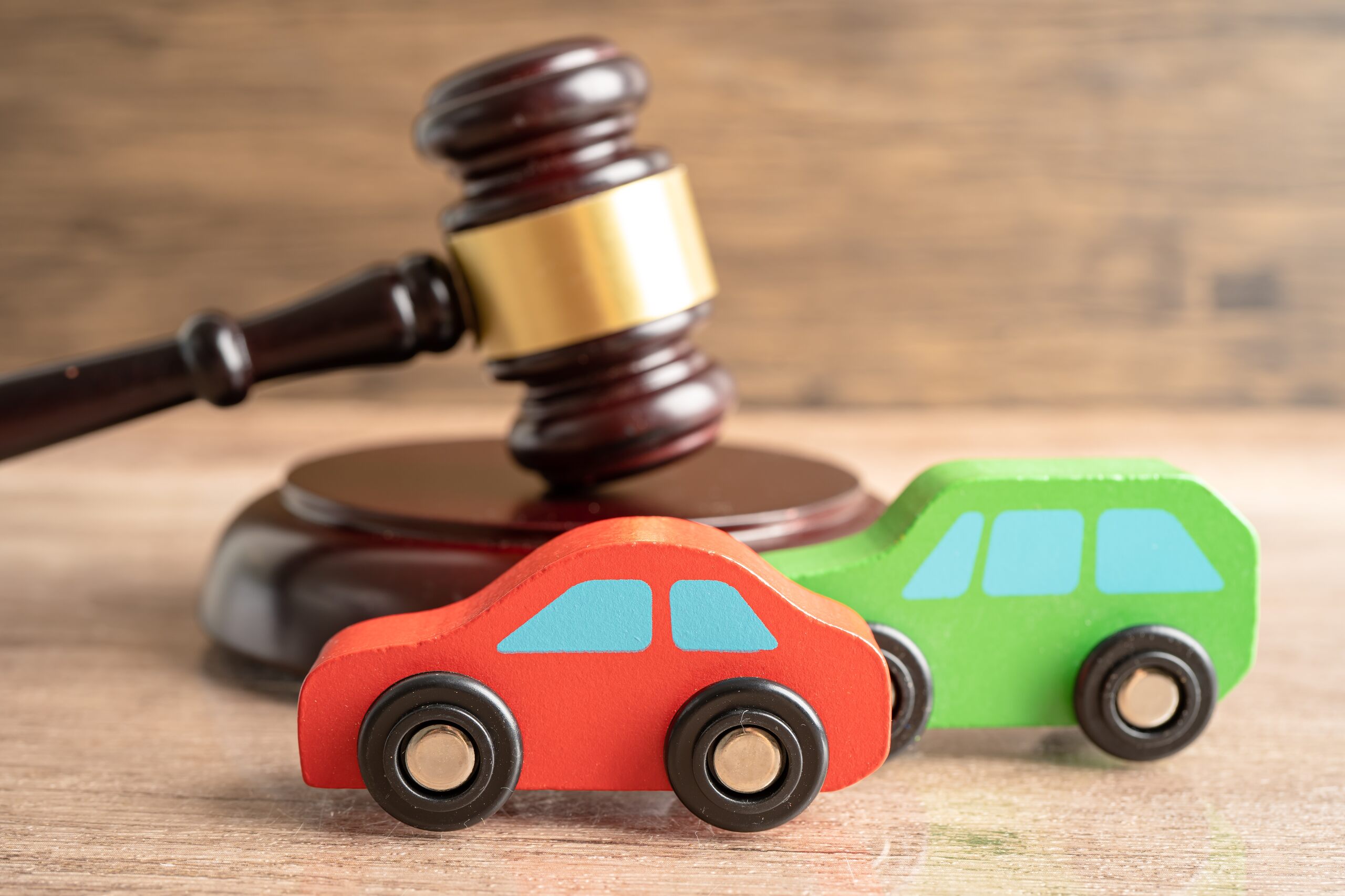 ed and green toy cars in front of a legal gavel, illustrating the difference between insurance notification and a formal statement after a Washington car accident.