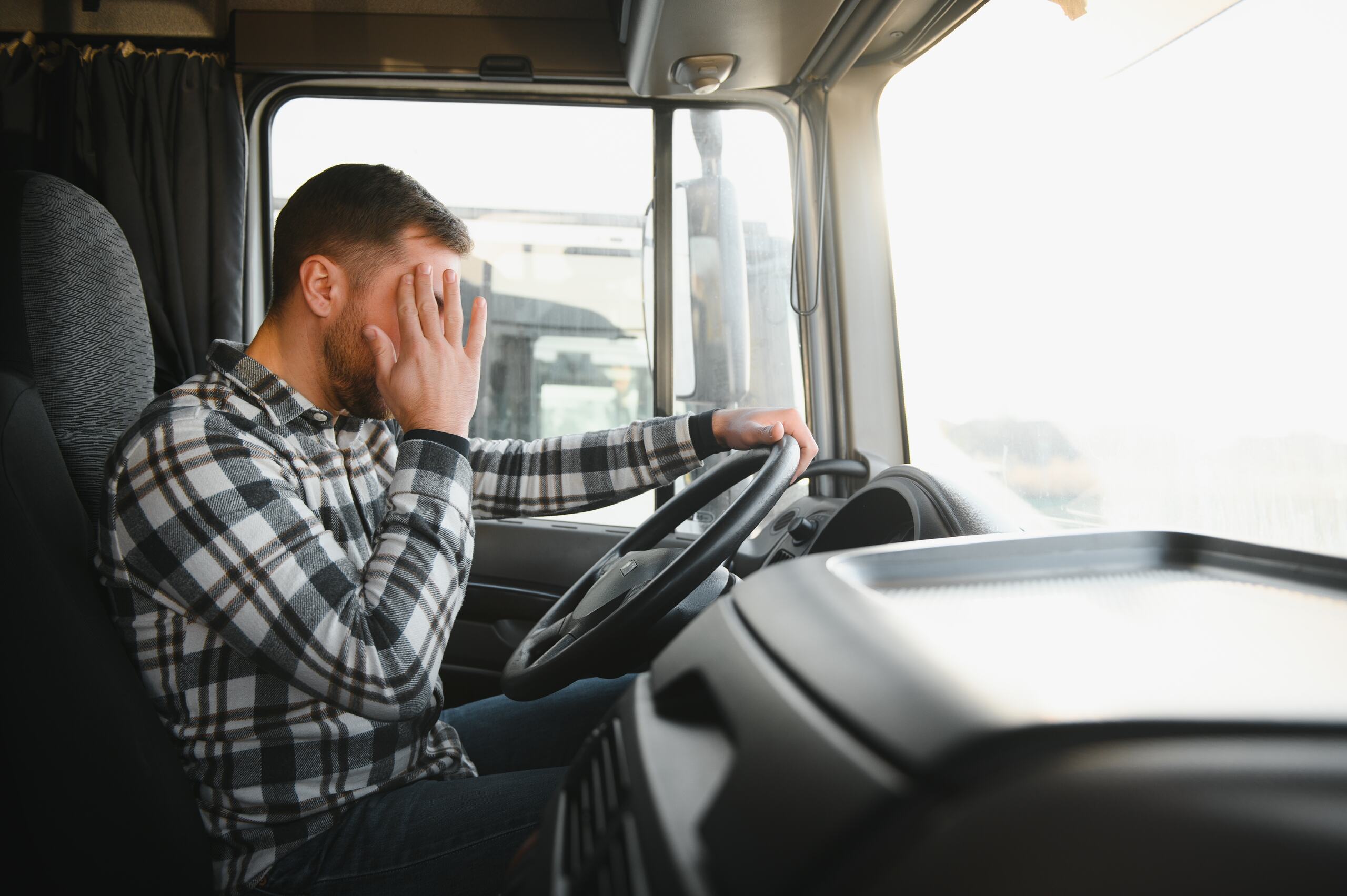 A fatigued truck driver rubbing his eyes while operating a semi-truck on I-90 near Spokane, illustrating the risk of drowsy driving.