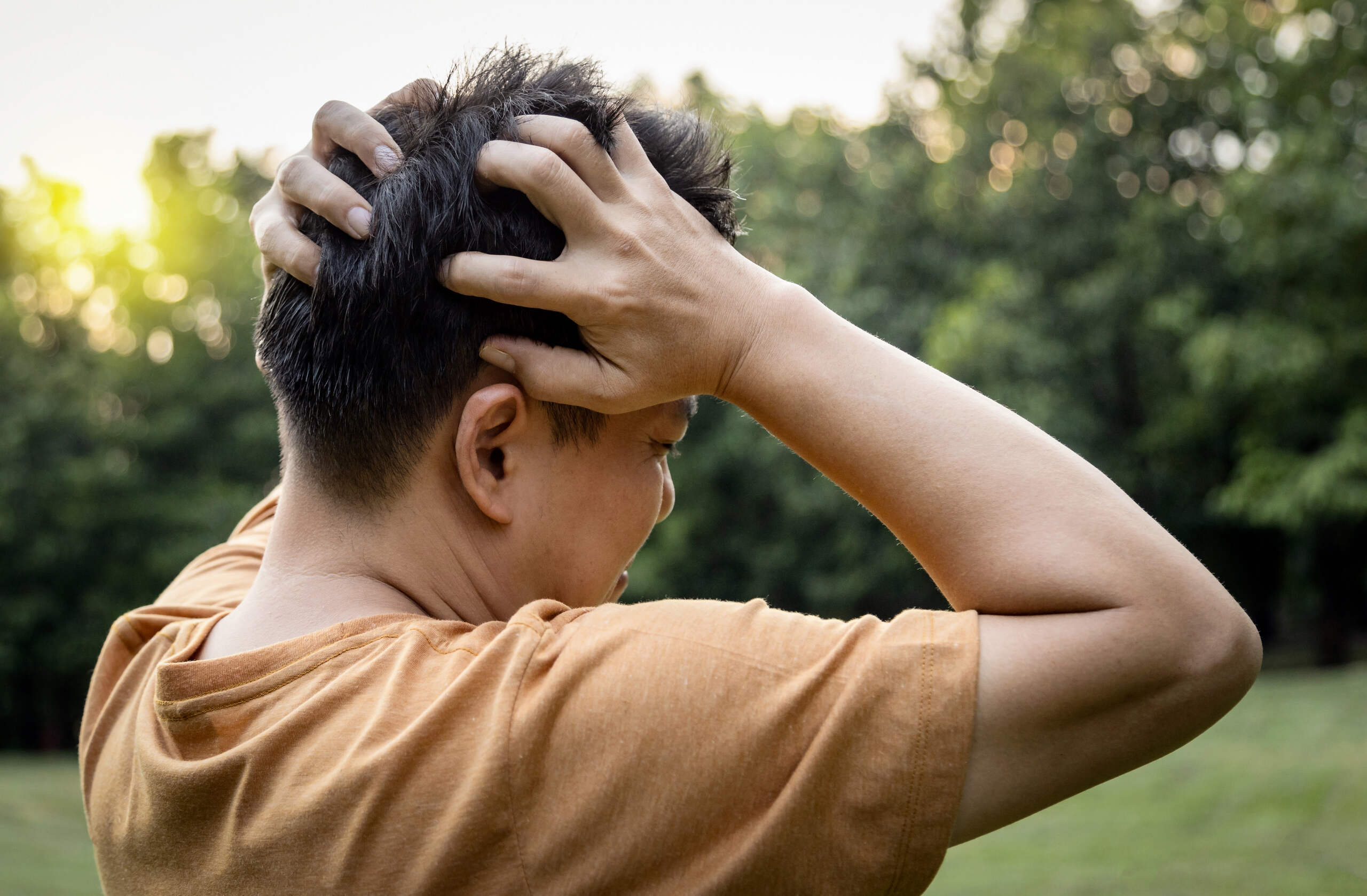 Close-up of person holding head in pain outdoors, illustrating symptoms of a mild concussion and need for a Spokane personal injury lawyer
