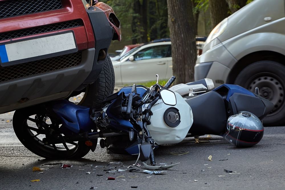 Wrecked motorcycle under a car bumper, showing the severity that separates real settlements from average statistics
