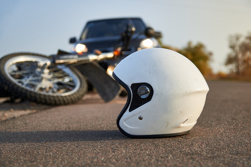 Motorcycle helmet on the road beside wreckage, illustrating the risks riders face from negligent drivers