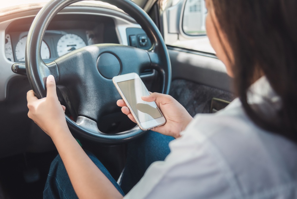 Driver texting behind the wheel, illustrating the insurance coverage gap between rideshare app periods